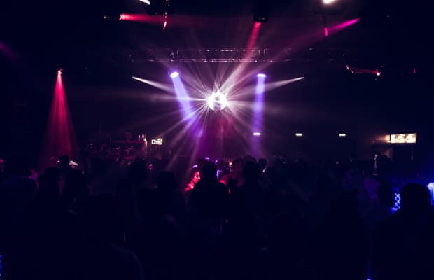 Foto einer Clubnacht, auf dem man schemenhaft Menschen im Dunkeln erkennt, über der Menge leuchtet eine Discokugel.