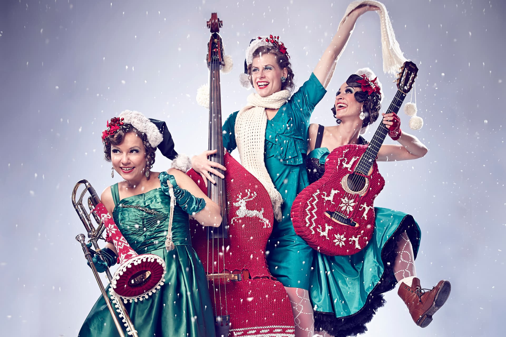 Die Musikerinnen der Zucchini Sistaz mit Kontrabass, Gitarre und Posaune in winterlich-weihnachtlicher Bühnenkleidung.