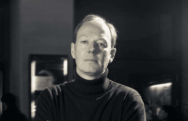 Schwarz/weiß-Porträt des Talk-Gasts Martin Sonneborn, der mit eiben schwarzen Rollkragenpullover ernst in die Kamera blickt.