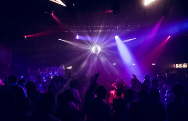 Foto einer Clubnacht, auf dem man schemenhaft Menschen im Dunkeln erkennt, über der Menge leuchtet eine Discokugel.