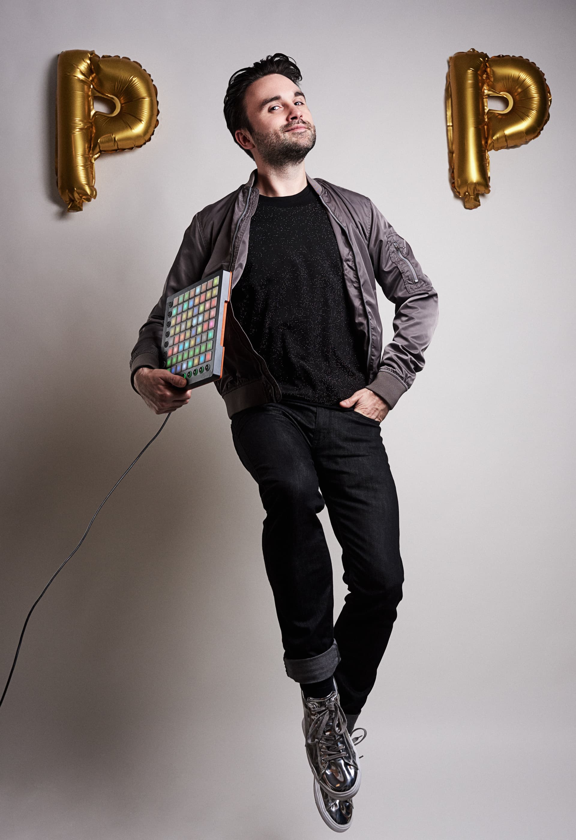 Dr. Pop steht mit einem Sampler-Gerät zwischen zwei goldenen Luftballons in der Form eines P. Sein Kopf in der Mitte wirkt wie das ‚O‘ in ‚POP‘.