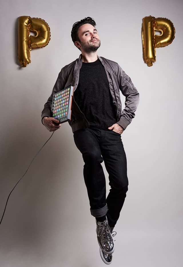 Dr. Pop steht mit einem Sampler-Gerät zwischen zwei goldenen Luftballons in der Form eines P. Sein Kopf in der Mitte wirkt wie das ‚O‘ in ‚POP‘.