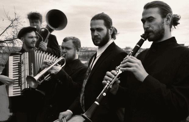 Schwarz-weiß Fotografie mit fünf Musikern in dunkler Kleidung mit ihren Instrumenten: Klarinette, Trommel, Trompete, Akkordeon und Tuba.