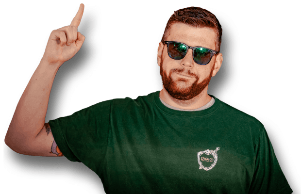 Porträt des Comediens mit grünem T-Shirt und Sonnenbrille; er blick frontal in die Kamera und zeigt mit angewinkeltem Arm und dem rechten Zeigefinger nach oben.