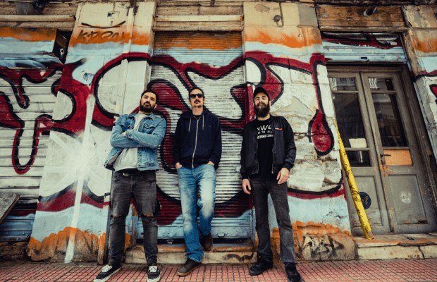 Von vorne und unten aufgenommenes Foto der Band, die lässig vor einer bunten Graffiti-Wand steht.