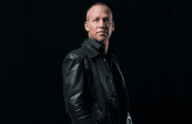 Der Jazzmusiker Avishai Cohen steht mit seitlichem Blick zur Kamera, trägt eine schwarze Lederjacke und ein dunkles Hemd. Der Hintergrund ist schwarz.
