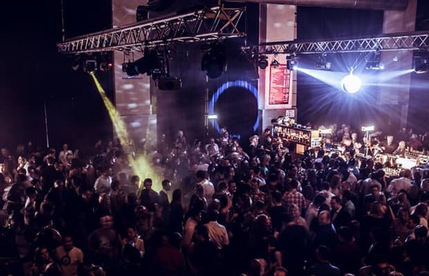 Foto einer Clubnacht, auf dem man viele Menschen im Dunkeln erkennt, über der Menge leuchtet eine Discokugel.