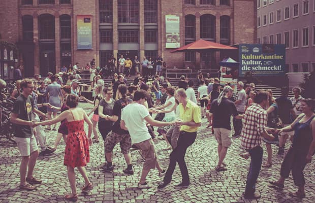 Tanzende Paare bei der Veranstaltung ‚Swing and Ride‘ auf einem Kopfsteinpflasterplatz vor der Centralstation, einem Gebäude mit roter Klinkerfassade.