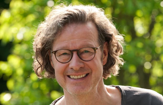 Michael Herd mit Brille lächelt in die Kamera, im sonnigen Naturhintergrund mit verschwommenem Grün.