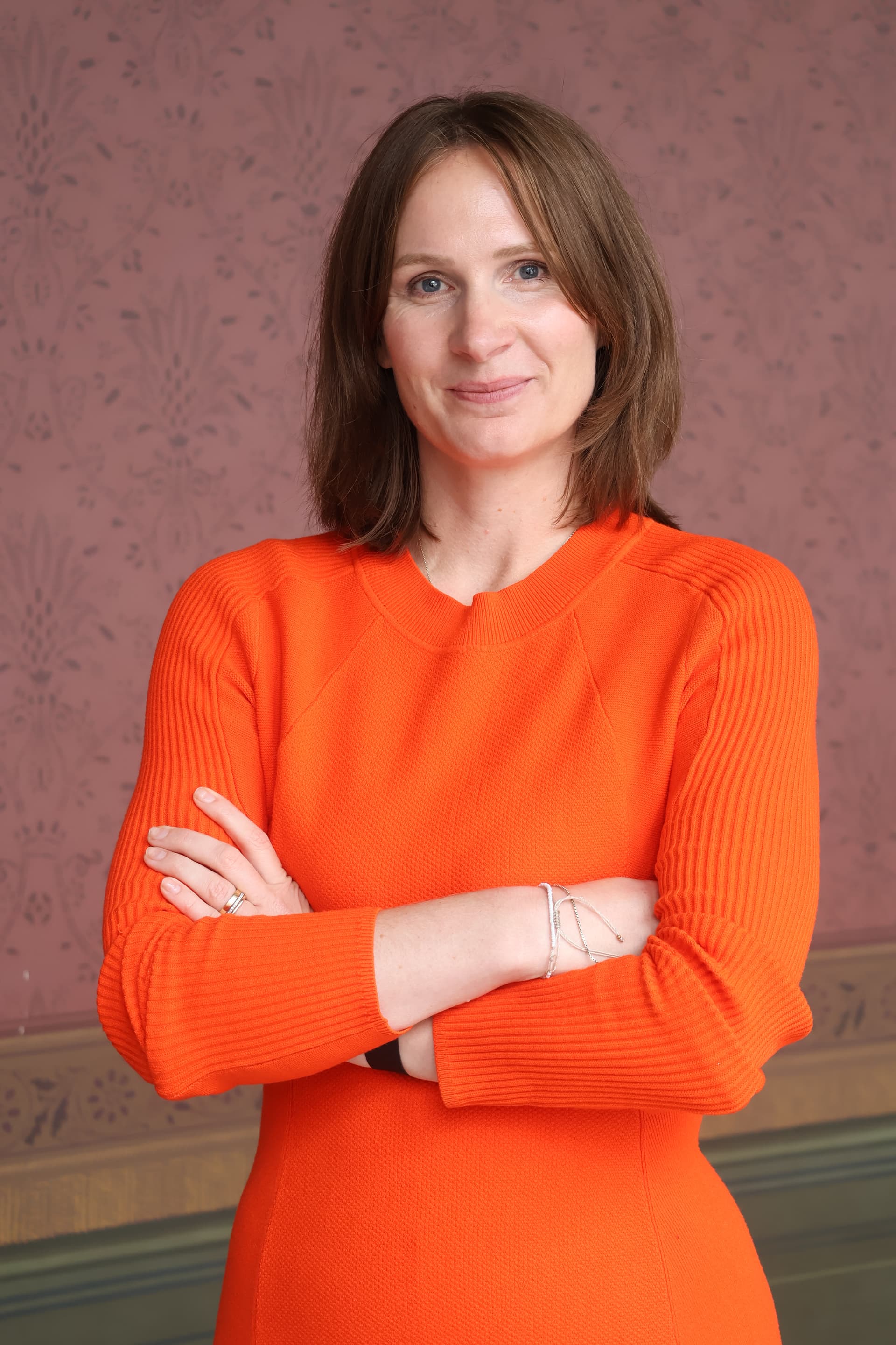 Miriam Zeleke, Referentin, trägt ein orangefarbenes Strickkleid und blickt lächelnd in die Kamera.