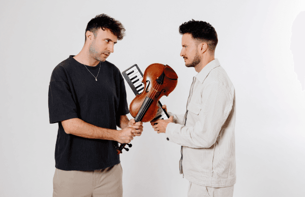 Zwei Männer stehen sich gegenüber und halten gemeinsam eine Geige und ein kleines Keyboard in den Händen.