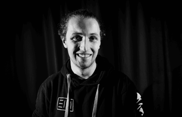 DJ Eidi trägt einen lässigen Kapuzenpullover, blickt frontal in die Kamera und lächelt. Das Foto ist schwarz-weiß.