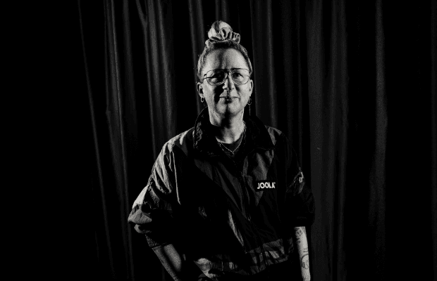 Djane Käry blickt in die Kamera. Sie trägt die Haare zum Dutt und eine sportliche Jacke. Die rechte Hand hat sie lässig in der Hosentasche. Das Foto ist schwarz-weiß.